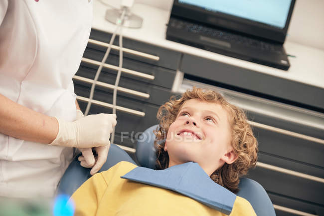 Женщина-врач в форме разговаривает с маленьким пациентом в кабинете дантиста — стоковое фото