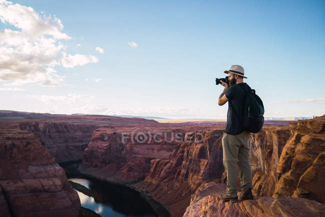 Vista laterale del ragazzo con lo zaino utilizzando la fotocamera fotografica per scattare foto di bellissimo canyon e fiume calmo sulla costa occidentale degli Stati Uniti — Foto stock