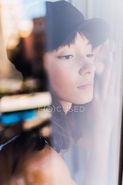 Vista através da janela da jovem mulher morena encantadora olhando para longe — Fotografia de Stock