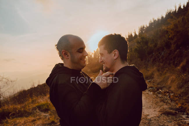 Laughing homosexual couple hugging on path in mountains in sunny day — Stock Photo