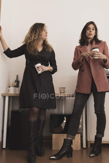 Vista lateral de jóvenes colegas alegres atractivos conversando y sosteniendo tazas de bebida cerca de la impresora en la oficina - foto de stock