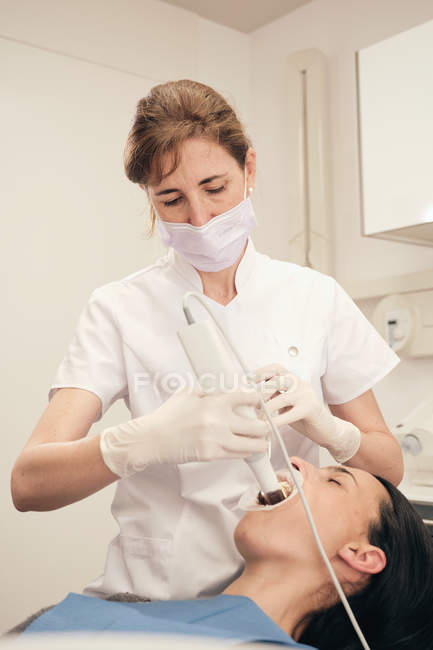 Frau in Handschuhen und Maske mit modernen Geräten zur Untersuchung der Zähne einer Patientin in der Zahnarztpraxis — Stockfoto