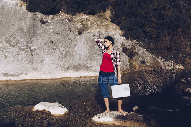 Mulher de pé na rocha com caso perto de água limpa no lago — Fotografia de Stock