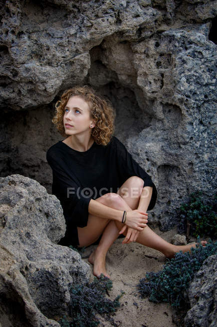Joven mujer pensativa sentada en las rocas y abrazando las rodillas - foto de stock