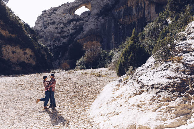 Jovem casal abraçando no cânion entre montanhas rochosas em dia ensolarado — Fotografia de Stock