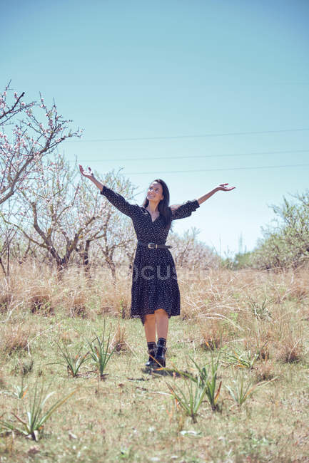 Joven mujer alegre en vestido de pie en el jardín con árboles frutales en flor - foto de stock