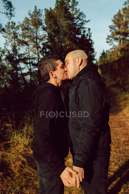 Glückliches homosexuelles Paar umarmt und küsst sich bei sonnigem Wetter auf der Strecke im Wald — Stockfoto