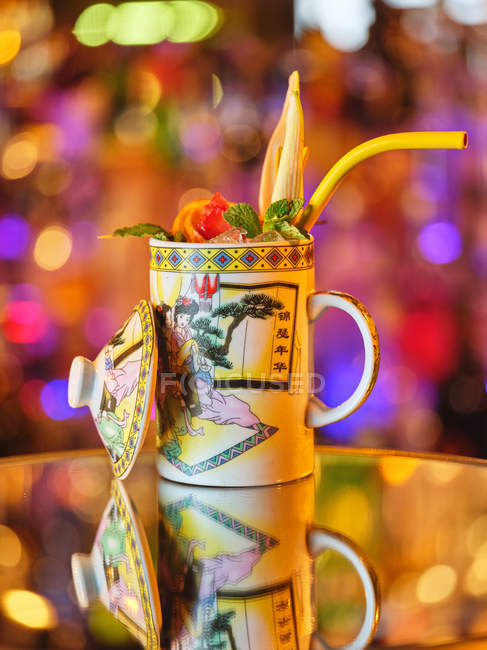 Ornamental mug of tasty cocktail decorated with exotic fruits and straw on table in bar — Stock Photo