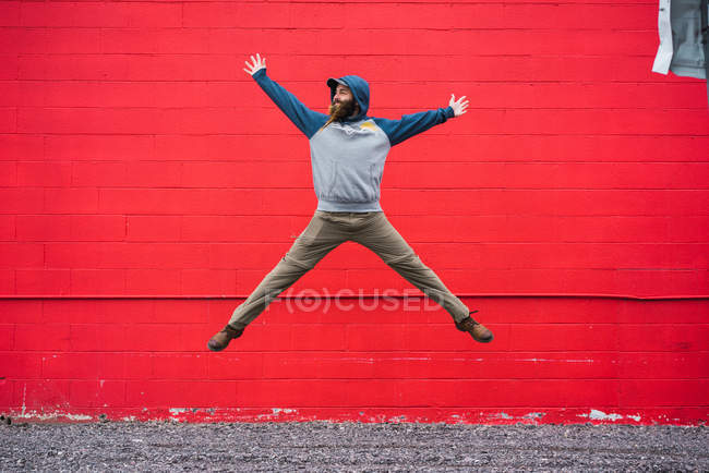 Handsome bearded male in casual outfit looking away while leaping up near red brick wall on city street — Stock Photo