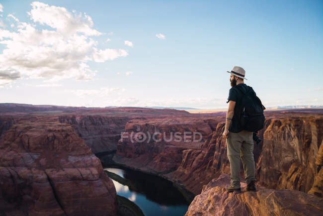 Seitenansicht von Kerl mit Rucksack, der Fotokamera am schönen Canyon und ruhigen Fluss an einem sonnigen Tag an der Westküste der USA hält — Stockfoto