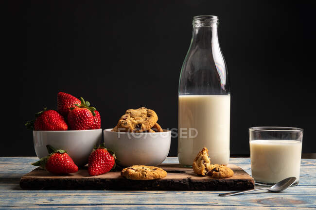 Vidro e garrafa de leite e pilha de biscoitos frescos em tábua de madeira perto guardanapo — Fotografia de Stock