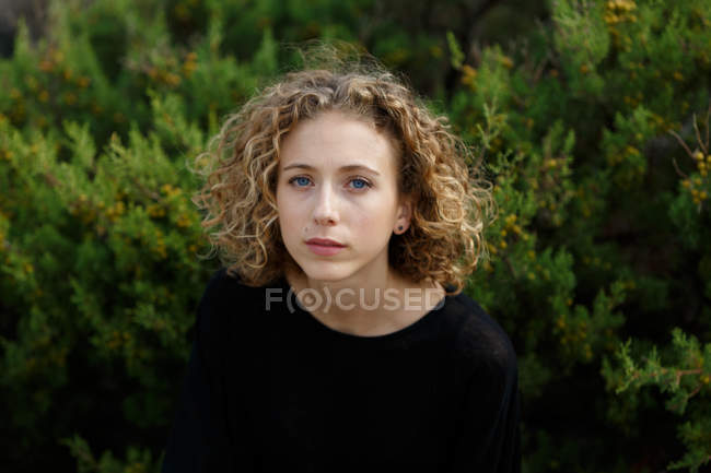 Porträt einer jungen, charmanten Frau mit blonden lockigen Haaren, die in der Natur in die Kamera schaut — Stockfoto