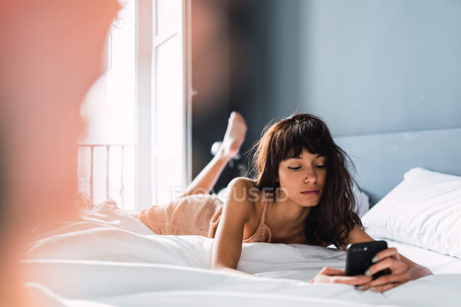 Молода жінка використовує мобільний телефон і спить на ліжку — стокове фото