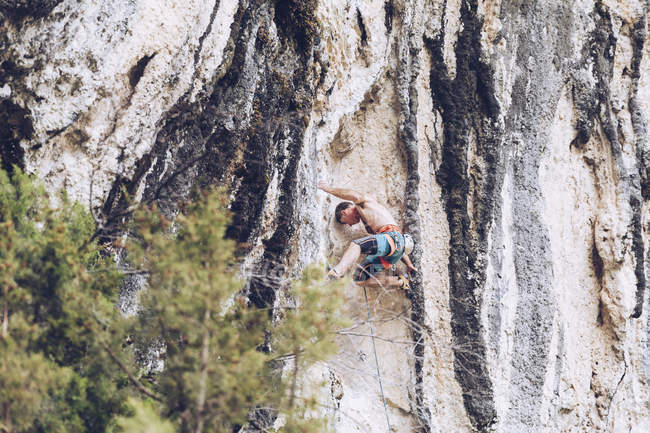 Vista laterale dell'uomo in pantaloncini arrampicata su ruvida falesia nella giornata di sole in campagna — Foto stock