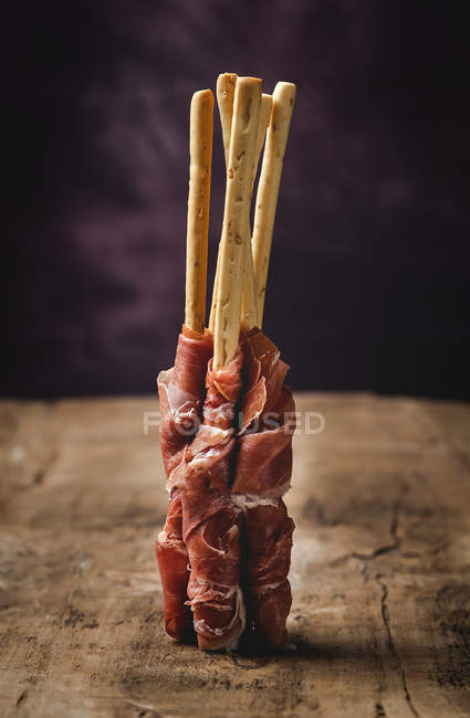 Gressinis with spanish typical serrano ham on wooden table on dark background — Stock Photo