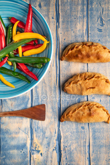 Hausgemachte Pasteten und frische grüne und rote Chilischoten auf blauem Teller auf grauem Holztisch — Stockfoto