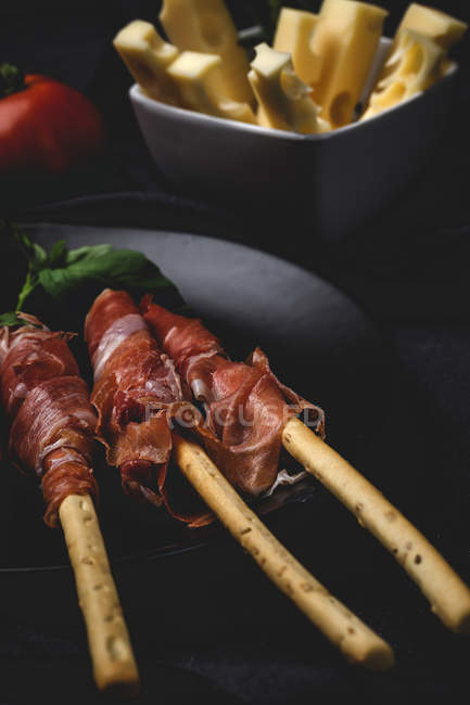 Gressinis with spanish typical serrano ham on plate with cheese on black background — Stock Photo