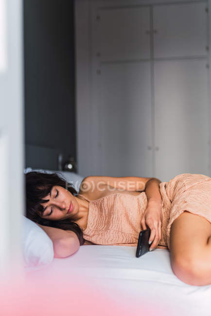 Jovem mulher usando telefone celular e descansando na cama — Fotografia de Stock