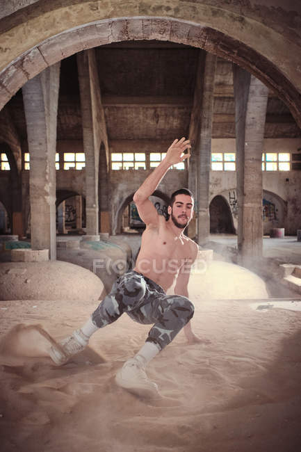 Shirtless young man dancing on sand indoors — Stock Photo
