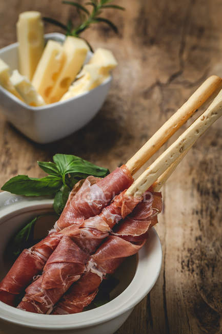 Gressini con tipico prosciutto serrano spagnolo in pentola su tavola di legno con formaggio — Foto stock
