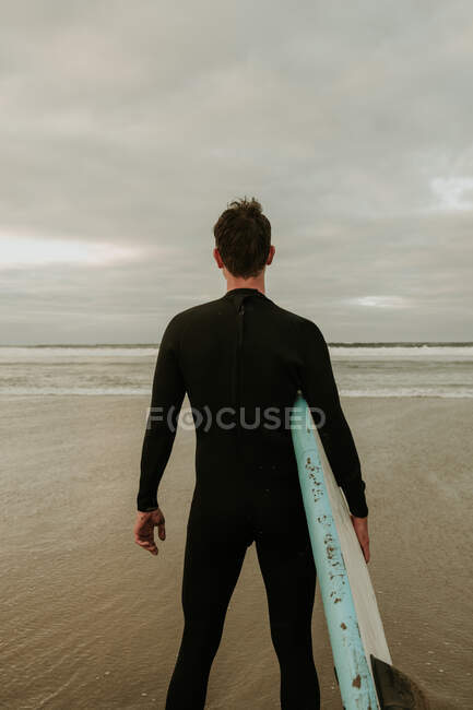 Persona con tabla de surf de pie cerca del mar - foto de stock