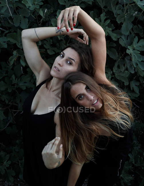 Seitenansicht attraktiver junger Frauen mit geschlossenen Augen und erhobenen Händen, die neben grünem Strauch stehen — Stockfoto