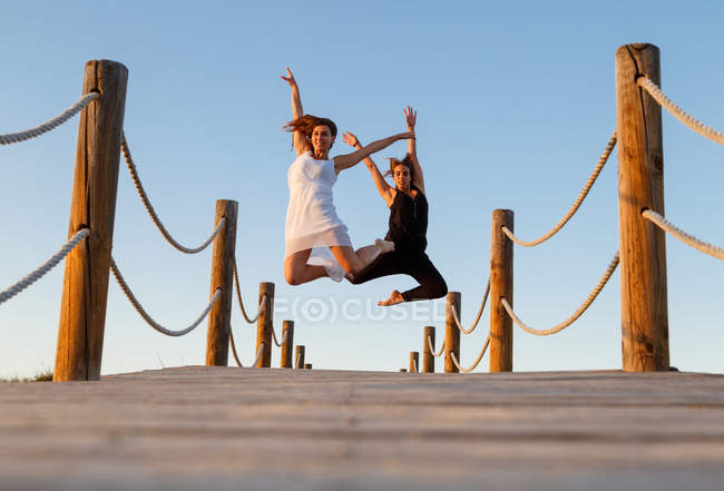 Junge Ballerinas in weiß-schwarzer Kleidung mit hochgestrecktem Bein in der Luft auf einem Steg und blauem Himmel bei sonnigem Tag — Stockfoto