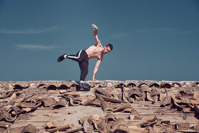 Man doing handstand on roof against blue sky — Stock Photo