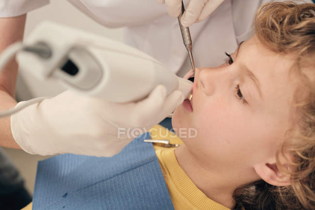 Manos del médico que hace la exploración de los dientes del niño pequeño mientras trabaja en la clínica del dentista - foto de stock