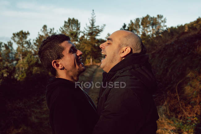 Rindo casal homossexual abraçando no caminho na floresta em dia ensolarado — Fotografia de Stock