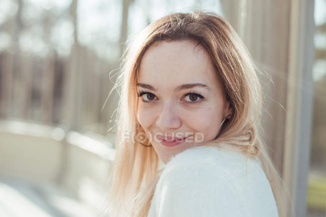 Стильна усміхнена молода жінка дивиться на камеру на сонячному світлі — стокове фото