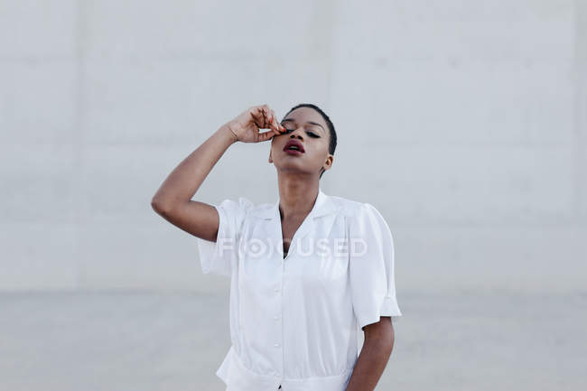 Mode femme ethnique aux cheveux courts en chemise blanche posant contre un mur gris — Photo de stock