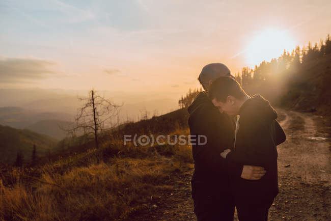Romantic homosexual couple hugging on path in mountains in sunny day — Stock Photo