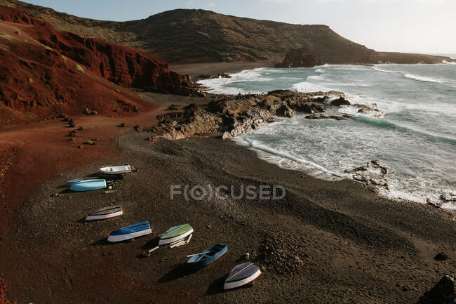 Modern boats located on rocky coast near waving sea and amazing hills on sunny day in wonderful countryside — Stock Photo