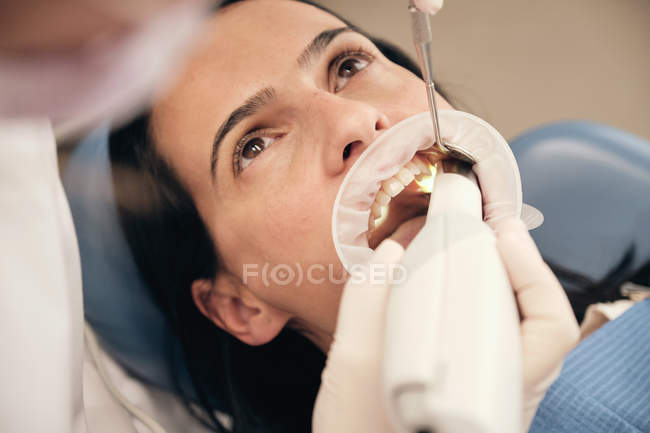 Mãos de dentista em luvas e máscara usando equipamento moderno para fazer a varredura de dentes de paciente feminino em consultório odontológico — Fotografia de Stock