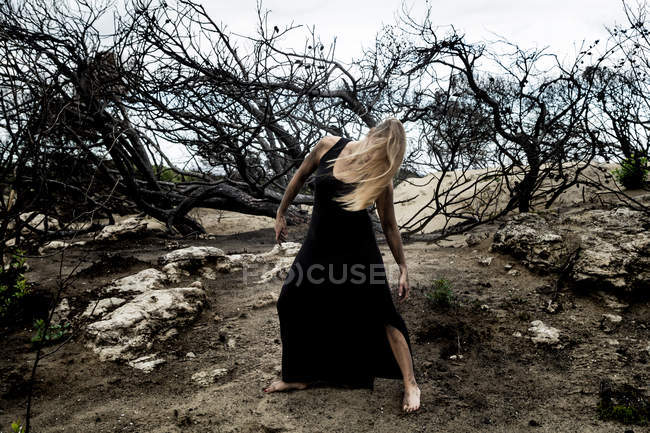 Молода балерина в чорному одязі танцює на суші між сухим лісом — стокове фото