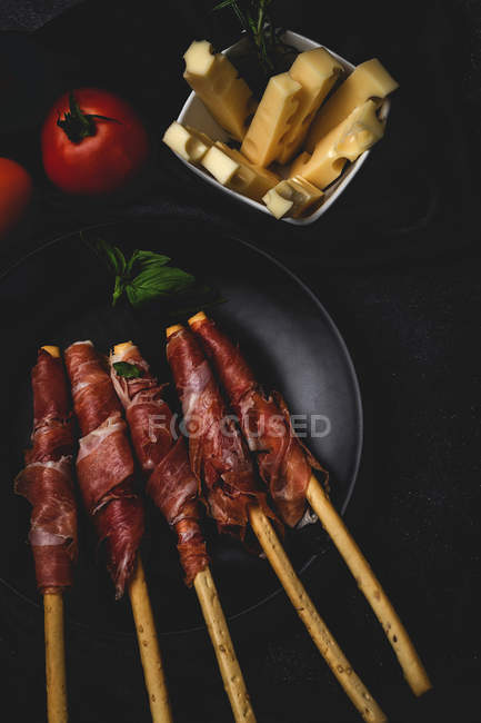 Gressini con prosciutto tipico spagnolo serrano su piatto nero con pomodori freschi e formaggio — Foto stock
