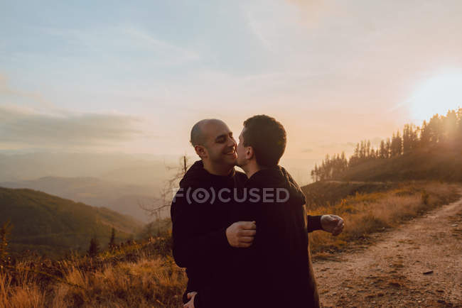 Romântico casal homossexual abraçando no caminho nas montanhas no dia ensolarado — Fotografia de Stock