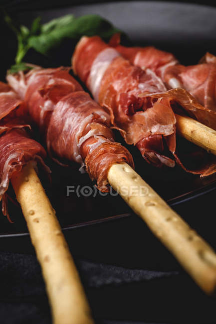 Gressini con tipico prosciutto serrano spagnolo su piatto su fondo scuro — Foto stock