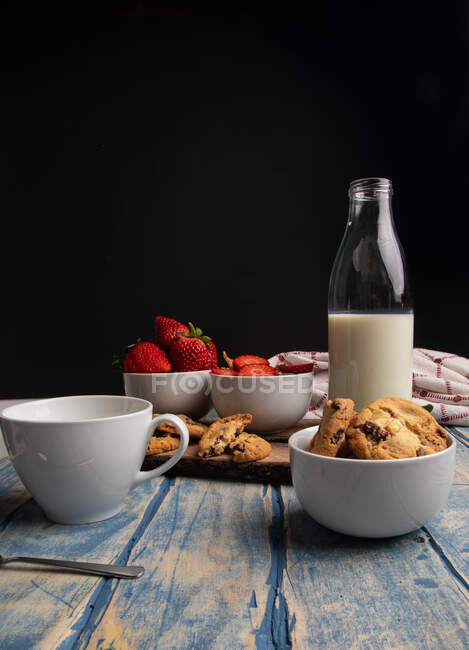 Vidro e garrafa de leite e pilha de biscoitos frescos em tábua de madeira perto guardanapo — Fotografia de Stock