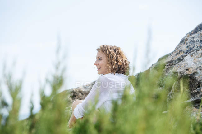 Joven mujer encantadora sentada entre roca y ramas - foto de stock
