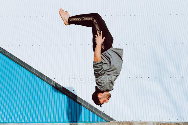 Barefoot guy in stylish outfit performing flip near wall of modern building — Stock Photo