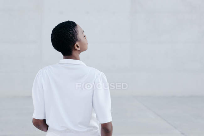 Back view of fashion short haired woman in white shirt posing against grey wall — Stock Photo