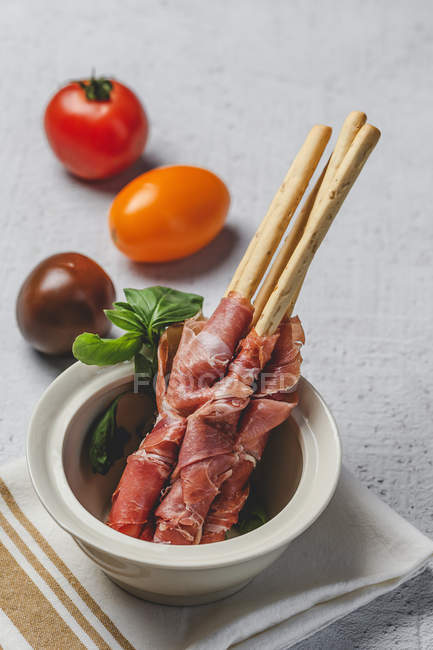 Gressini con tipico prosciutto serrano spagnolo in pentola e pomodori freschi su fondo bianco — Foto stock