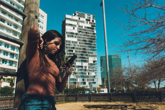 Дівчина-підліток дивиться на свій смартфон на вулиці в сонячний день — стокове фото