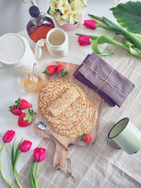 Desayuno con tortitas y fresas en la mesa de la cocina con flores - foto de stock