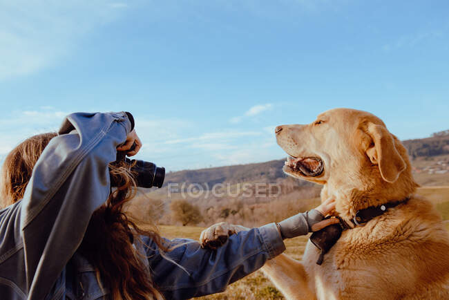 Vista lateral da jovem mulher atirando na câmera cão engraçado entre o prado e o céu azul — Fotografia de Stock