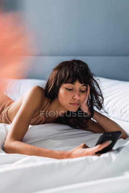 Jeune femme utilisant le téléphone portable et se reposant sur le lit — Photo de stock