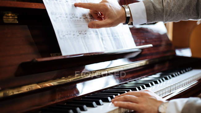 Recorte vista lateral de las manos del hombre tocando el piano en un estudio de música - foto de stock