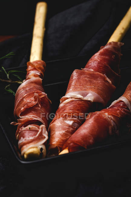 Gressini con tipico prosciutto serrano spagnolo su piatto su tessuto nero — Foto stock
